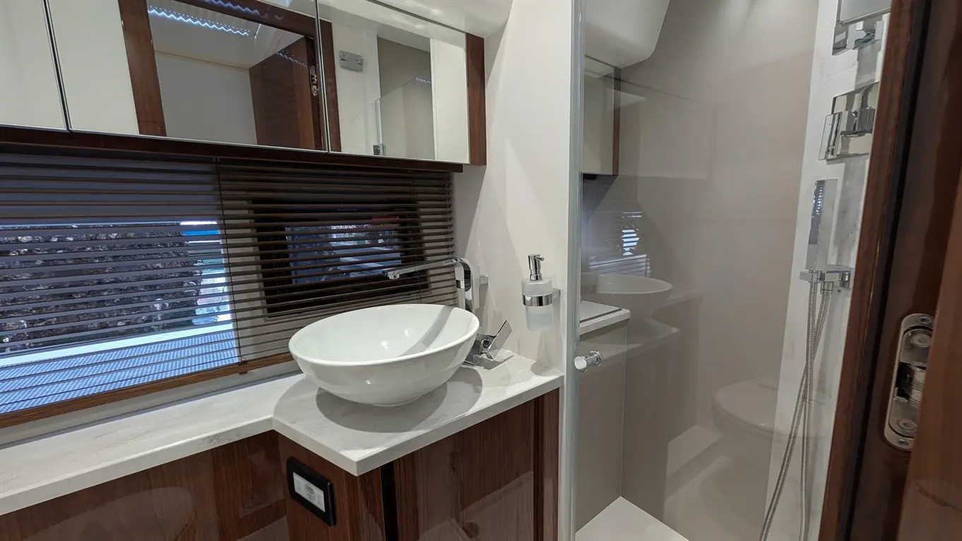 Modern bathroom featuring a white basin, marble countertop, and shower cubicle, with wooden cabinetry and natural light.